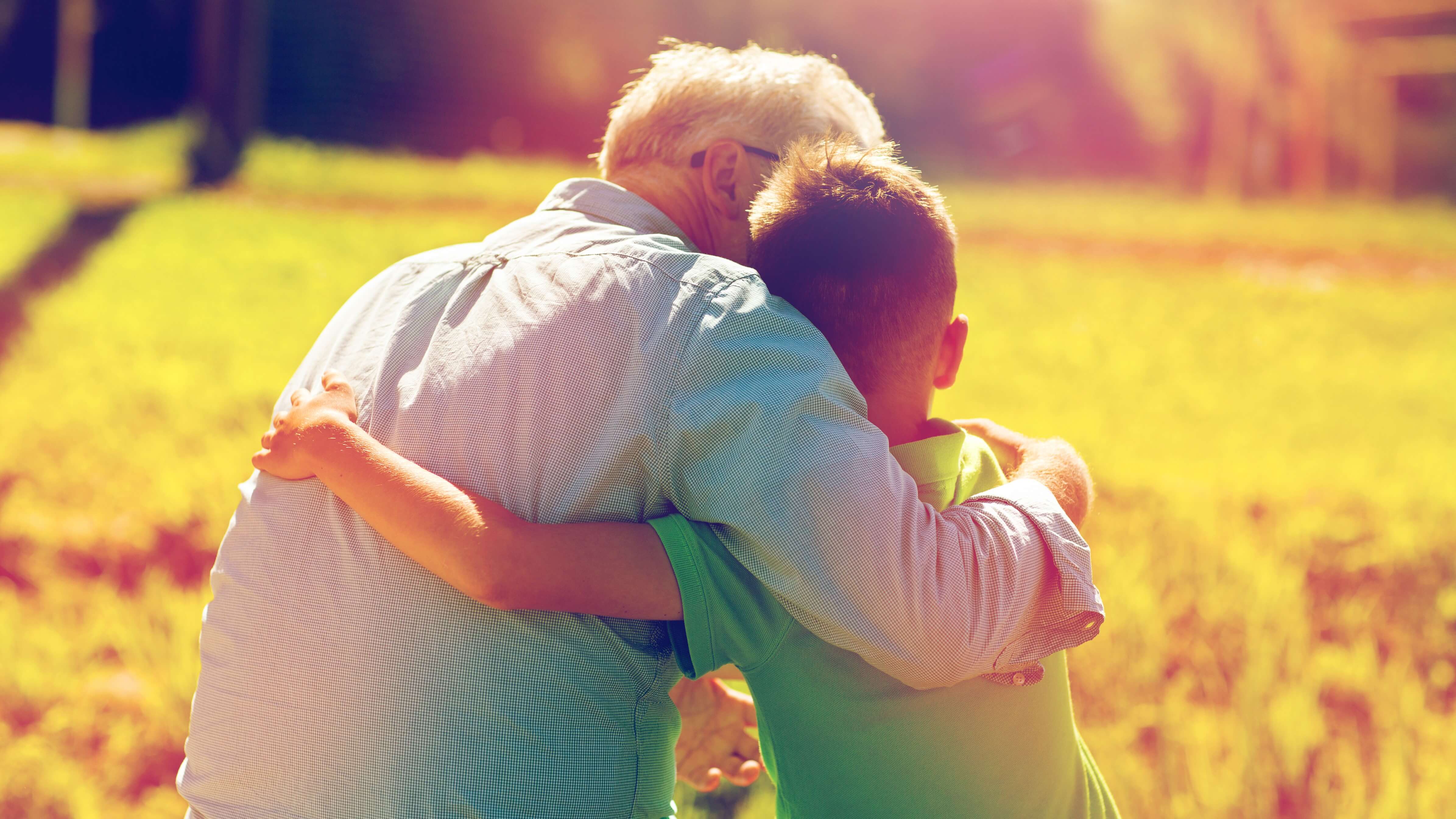 Young man and grandfather hugging outdoors